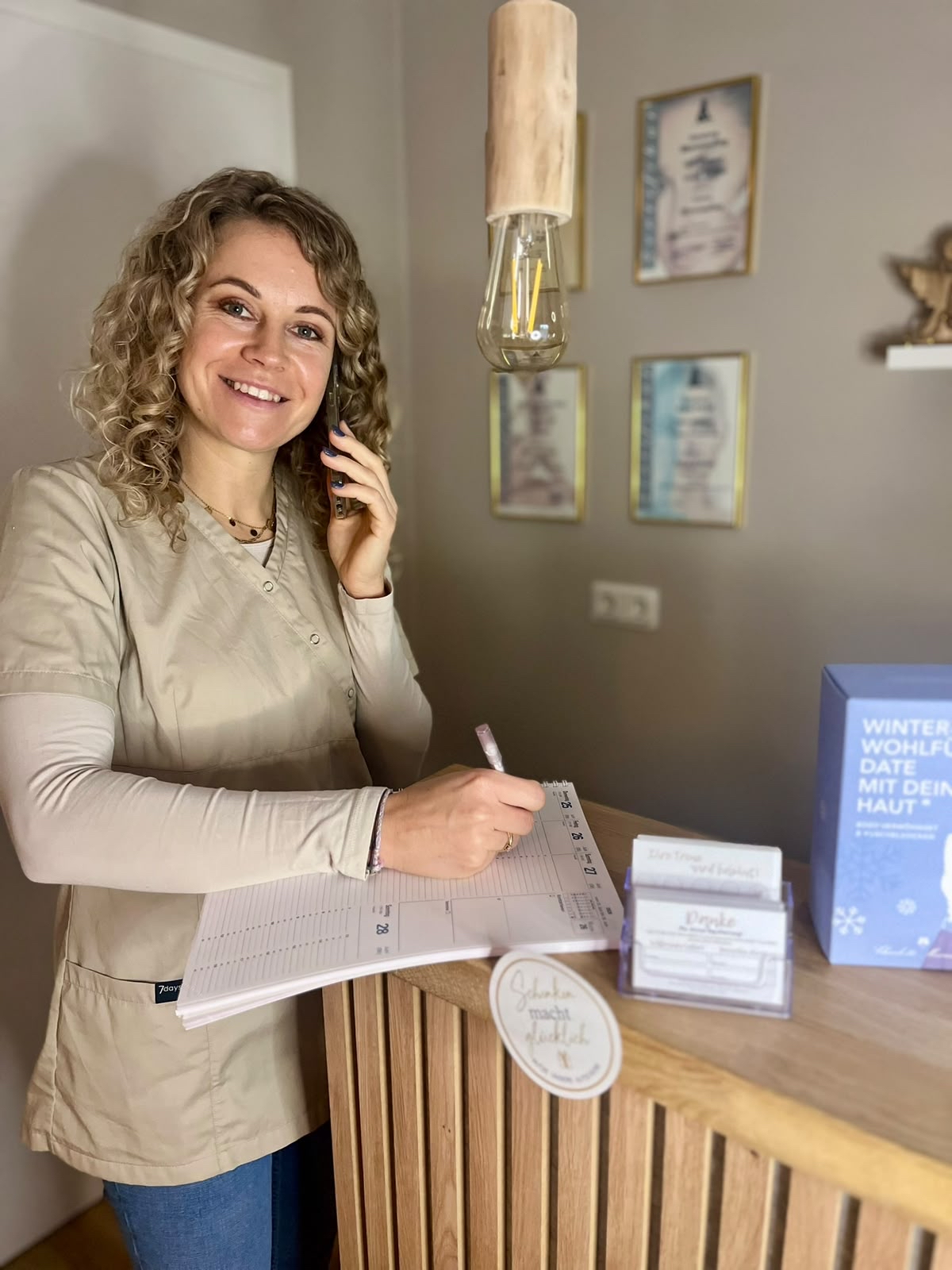 Laechelnde Frau mit lockigem Haar telefoniert und macht Termine am Empfang